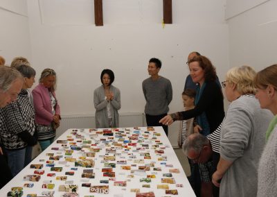 Künstler Café mit Nan Hirose und Kazuma Nagatani, Besucher stehen um einen Tisch mit Exponaten von den Künstlern